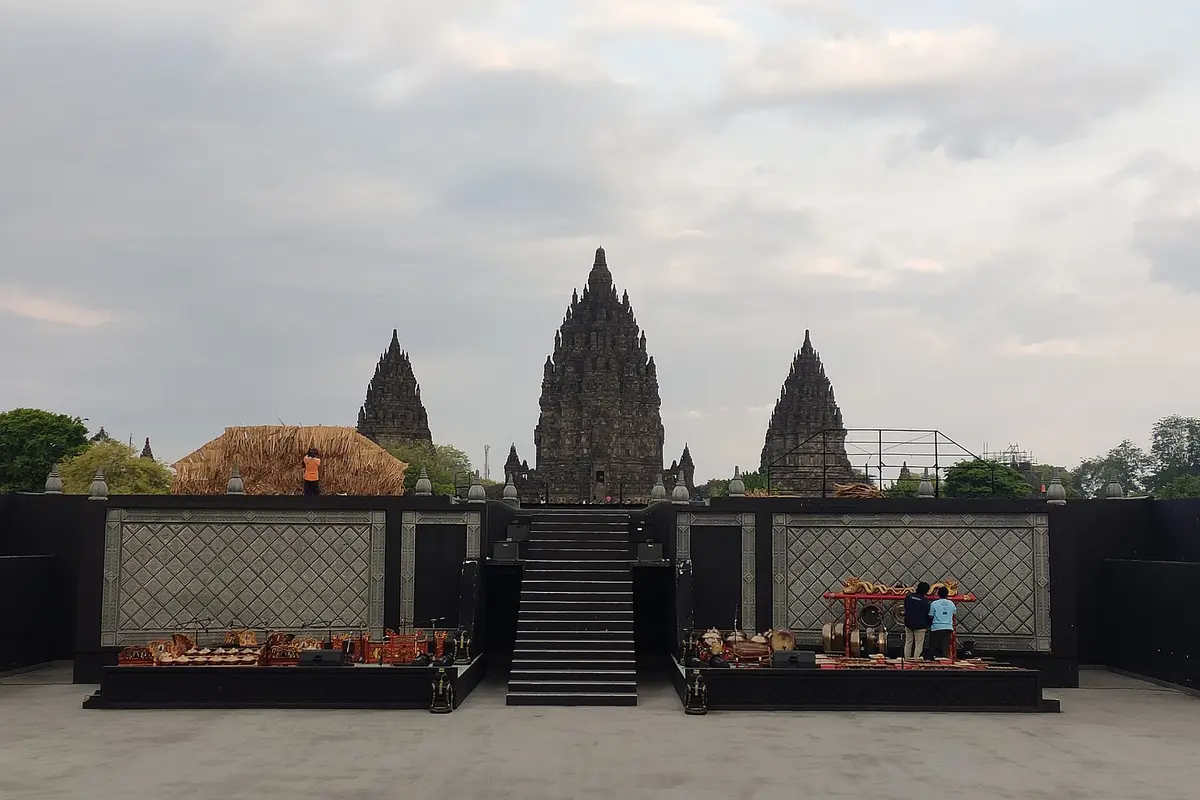 The empty open-air Ramayana Ballet stage in daylight, with gamelan instruments set out at each side and the three main Prambanan temples rising behind